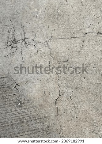 a photography of a fire hydrant sitting on the side of a road, concrete surface with cracks and cracks on it.
