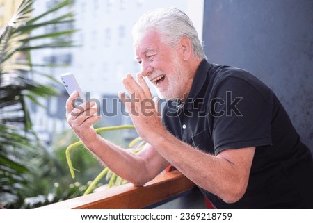 Handsome smiling bearded senior man using mobile phone webcam to communicate in video chat enjoying carefree moments with distant family or friends