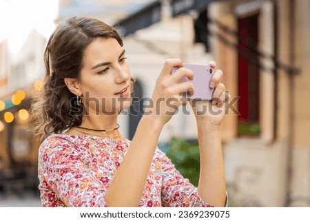 Caucasian young woman taking photography pictures of old city buildings outdoors. Adult girl blogger using smartphone photography app making photos for social media standing in street. Town lifestyles