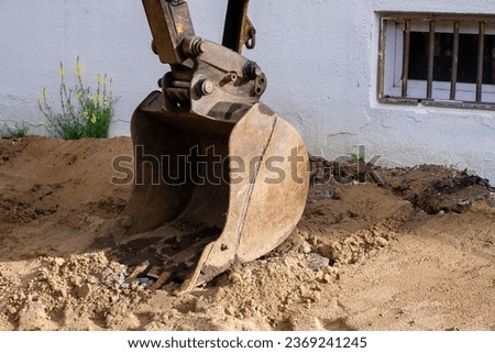 Excavator bucket on the sand with gravel of a construction site against the background of a house wall Royalty-Free Stock Photo #2369241245