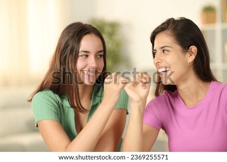 Two happy friends making pinky promise sitting at home Royalty-Free Stock Photo #2369255571