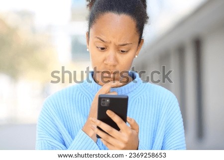 Front view portrait of a worried black woman checking phone in the street Royalty-Free Stock Photo #2369258653
