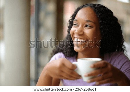 Happy black woman drinking coffee and laughing looking at side in a restaurant terrace Royalty-Free Stock Photo #2369258661