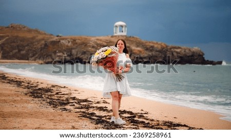 A girl with long hair in a white dress and a large bouquet of flowers, against the background of the sea.