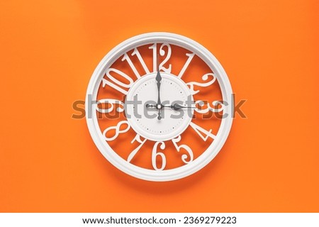 Modern white clock with a circle on a orange wall background, three o'clock on the clock. Elegant clock, combination of white and orange colors