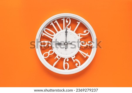 Modern white clock with a circle on a orange wall background, nine o'clock on the clock. Elegant clock, combination of white and orange colors