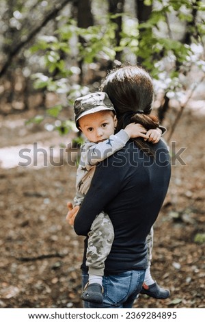 Young woman, mother holding a beautiful little child, son in a khaki cap, walking through the forest outdoors. Photography, portrait.