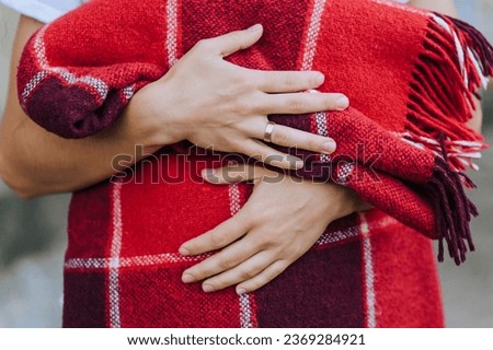 A woman holds in her hands a warm blanket, a checkered red plaid in the fall. Photography, portrait.