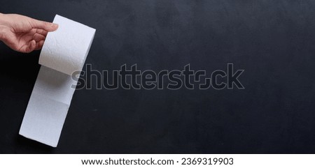 A female hand holds a roll of white toilet paper against a black background. Copy space