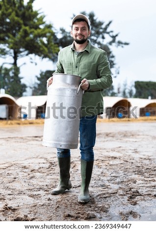 Portrait of positive man farm worker with big milk can posing outdoors on dairy farm Royalty-Free Stock Photo #2369349447
