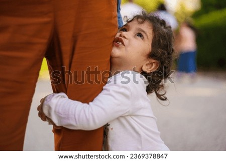 Young Mixed-Ethnicity Girl Embracing Mother's Leg - A 3-year-old girl with curly hair of Italian-Brazilian descent hugs her mother's leg tightly, capturing an intimate and tender moment. Royalty-Free Stock Photo #2369378847