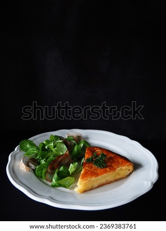 Homemade french potato pie with green salad, bacon and mushroom on the side, white plate, black background, vertical picture