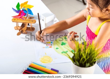 Asian cute kid preschooler sit on table smiling she draw picture with pencil at home, Happy child little girl colorful drawing family standing hold hands on planet earth on paper, earth day concept