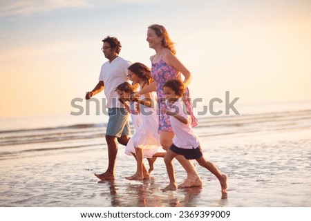 Family with kids walking on tropical beach at sunset. Cute little kids running with parents. Travel with kid. Summer vacation on sea shore. Family holiday with children. Water sport fun.
