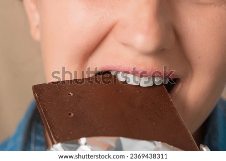 Close-up of a Caucasian woman's mouth biting a chocolate bar. Front view. Low angle view.