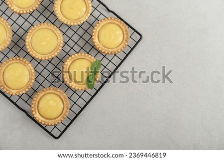 Mini tarts with  lemon and custard  filling on black metal cooling rack on kitchen table, top view