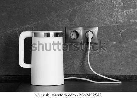 Electric kettle plugged into power socket on dark grey wall indoors Royalty-Free Stock Photo #2369452549