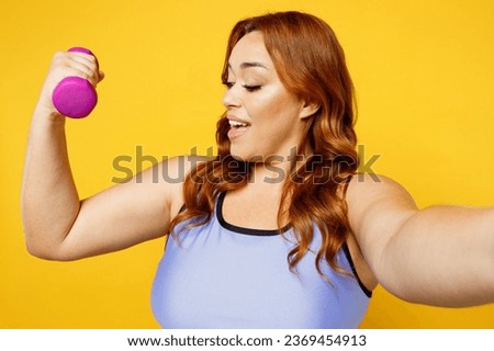 Close up young plus size big fat fit woman wears blue top warm up train do selfie shot pov on mobile cell phone hold muscles isolated on plain yellow background studio home gym. Workout sport concept