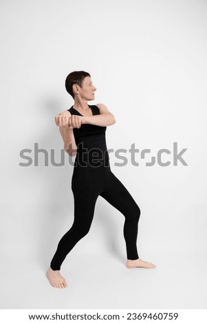 Athletic mature woman dressed in black, miming the sporty gesture of baseball