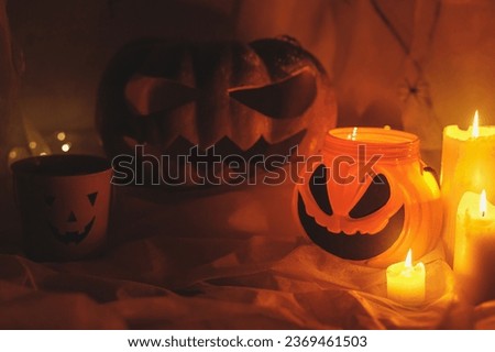 Happy Halloween! Spooky Jack o lantern carved pumpkin, spider web, candy bucket, spiders and glowing light in dark. Scary atmospheric halloween party decorations. Trick or treat