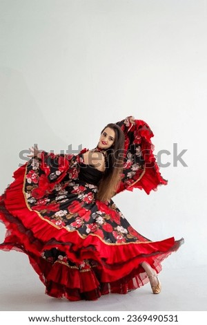 A young girl demonstrates a smart elegant red dress. Flamenco clothing. Gypsy romale style. Professional dancer isolated on white background. Royalty-Free Stock Photo #2369490531