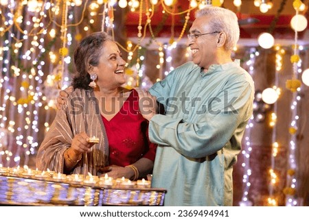 Happy Senior couple decorating with Diya on the occasion of Diwali festival celebration.