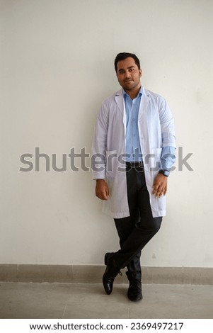 Portrait of south asian young doctor in white apron standing in front of a white background  Royalty-Free Stock Photo #2369497217