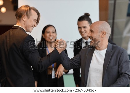 Young multiethnic collaborative process of professional businesspeople arm wrestling after new business contract signed with happy smiling face. Coworker and working together concept
