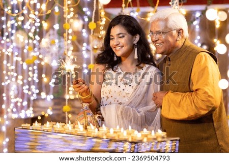 Happy grandfather and granddaughter playing with sparkler crackers on the occasion of Diwali festival celebration.