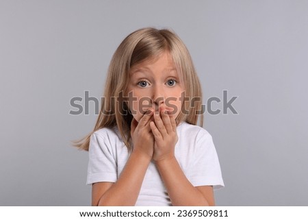 Embarrassed little girl covering mouth with hands on grey background Royalty-Free Stock Photo #2369509811