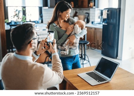 Proud father take picture of his wife with infant baby at home. Happy family, technology concept.