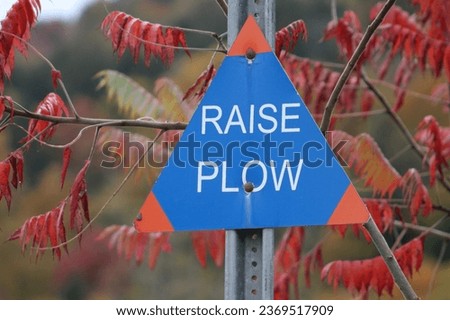 A triangle shaped sign that says "raise plow".