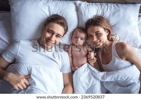 Portrait of beautiful young parents and cute baby looking at camera and smiling while lying together in bed