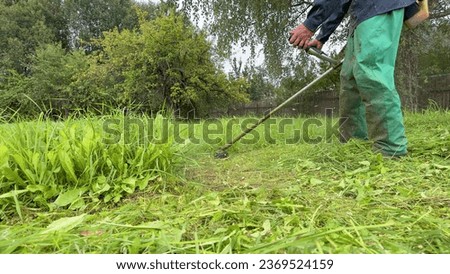 Gardener mows weeds grass. Man cutting grass in yard by using string trimmer. Worker lawn mower cutting green garden. Lawn mowing machine. Grass Trimmer and Grass Cutter. lawn maintenance service. Royalty-Free Stock Photo #2369524159