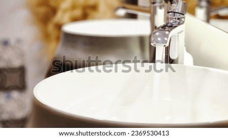 Running water tap spills water in wash basin. Cleaning, hygiene, economical usage of water, additional costs, water expenses, household budget