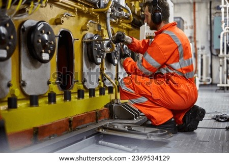 Engineer manually removes inspection covers to check condition of main engine pistons and bearing. Royalty-Free Stock Photo #2369534129