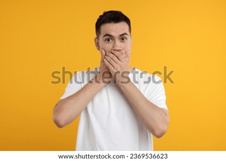 Embarrassed man covering mouth with hands on orange background Royalty-Free Stock Photo #2369536623