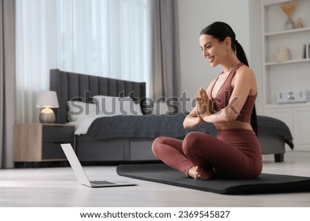 Beautiful young woman practicing Padmasana while watching online class on yoga mat at home, low angle view. Lotus pose