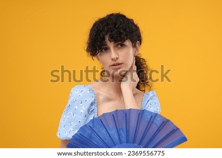 Woman with hand fan suffering from heat on orange background