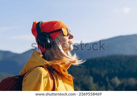 Cute smiling young woman with headphones on her head listening to the music in the mountains. Side view portrait of a relaxed woman meditating Royalty-Free Stock Photo #2369558469