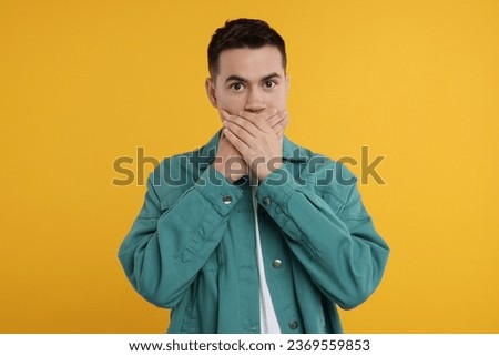 Embarrassed man covering mouth with hands on orange background Royalty-Free Stock Photo #2369559853