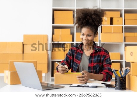 African woman selling online products over the internet sitting on sofa at home, enjoying the moment with cardboard box out of parcel, feeling happy about delivery.