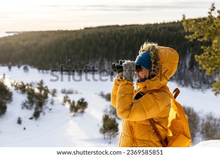 Young woman in yellow looking through binoculars at birds on snowy river against winter forest Birdwatching, zoology, ecology Research in nature, observation of animals Ornithology copy space Royalty-Free Stock Photo #2369585851