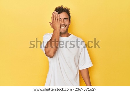 Young Latino man posing on yellow background having fun covering half of face with palm.