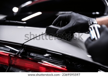 Employee of a car detailing studio or car wash applies a ceramic coating to the paint of a gray car Royalty-Free Stock Photo #2369595597