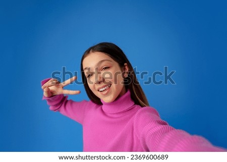 Portrait of a smiling teen girl making selfie photo on blue background
