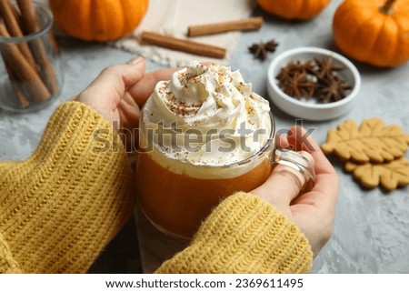 Woman holding cup of pumpkin spice latte with whipped cream at light grey table, closeup Royalty-Free Stock Photo #2369611495