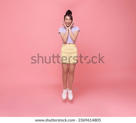 Happy Asian teen woman smiling and jumping while celebrating success isolated on pink background.