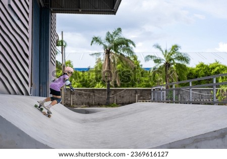 asian child skater or kid girl playing skateboard or ride surf skate on wave ramp or wave bank to fun top turn surfskate in skate park by extreme sport surfing to wears helmet knee guard body safety Royalty-Free Stock Photo #2369616127