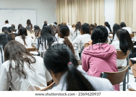 Rear view of college students concentrating on doing examinations in the classroom